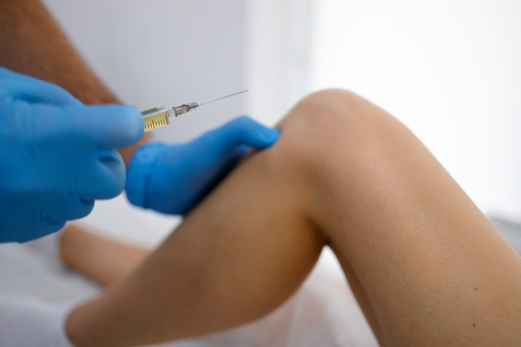 Close up view pf doctor hands with syringe injects plasma into a inflamed female knee for arthrosis and arthritis, plasma lifting procedure