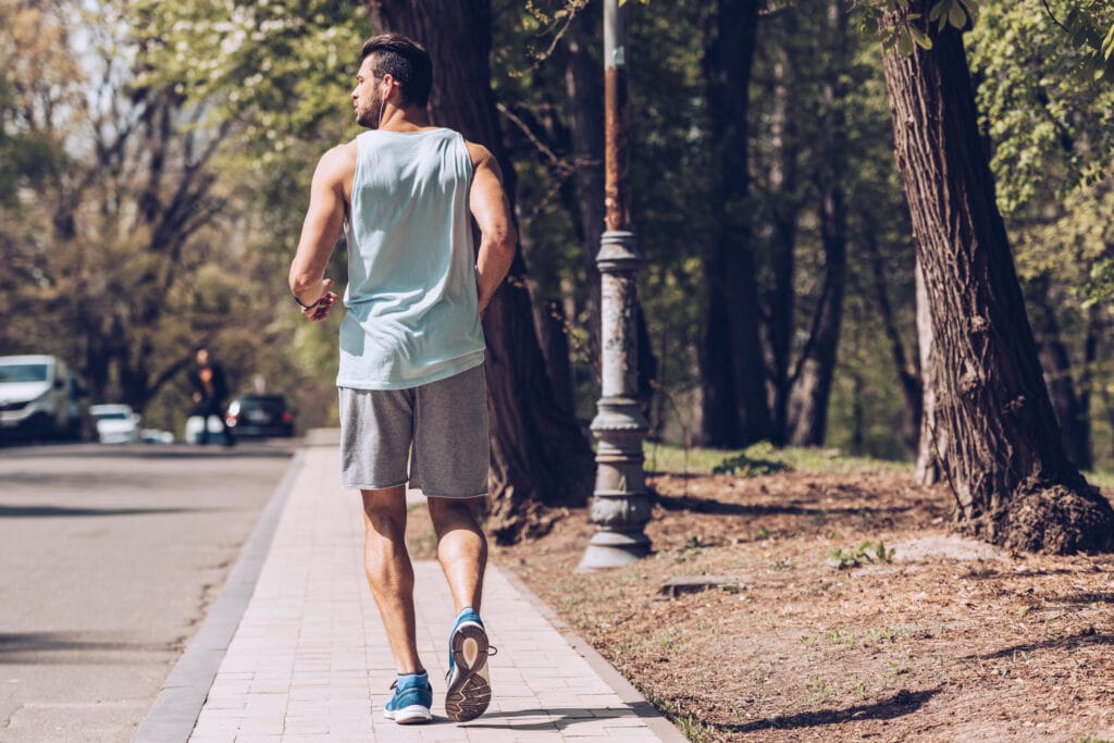 back view of young sportsman running along pavement near roadway